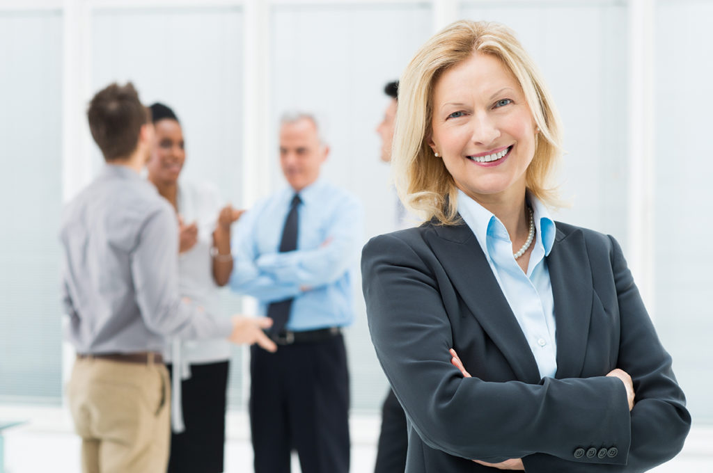 photo of smiling senior businesswoman in office with colleagues