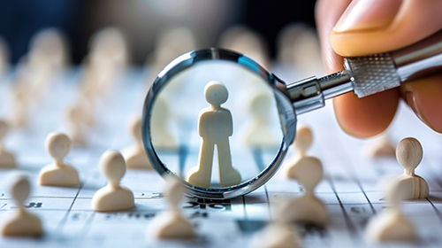 small figures meant to symbolize employees with magnifying glass singling out one employee